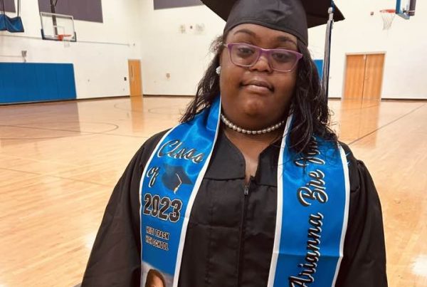 Female student with Down syndrome poses in graduation cap and gown.
