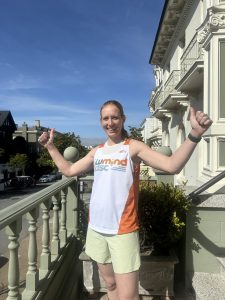 Woman stands on a balcony giving a thumbs up sign wearing a LuMind IDSC singlet.